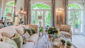 Un salon spacieux avec un canapé beige, une table basse et une vue sur une végétation luxuriante, visible à travers de grandes fenêtres en arc de cercle.