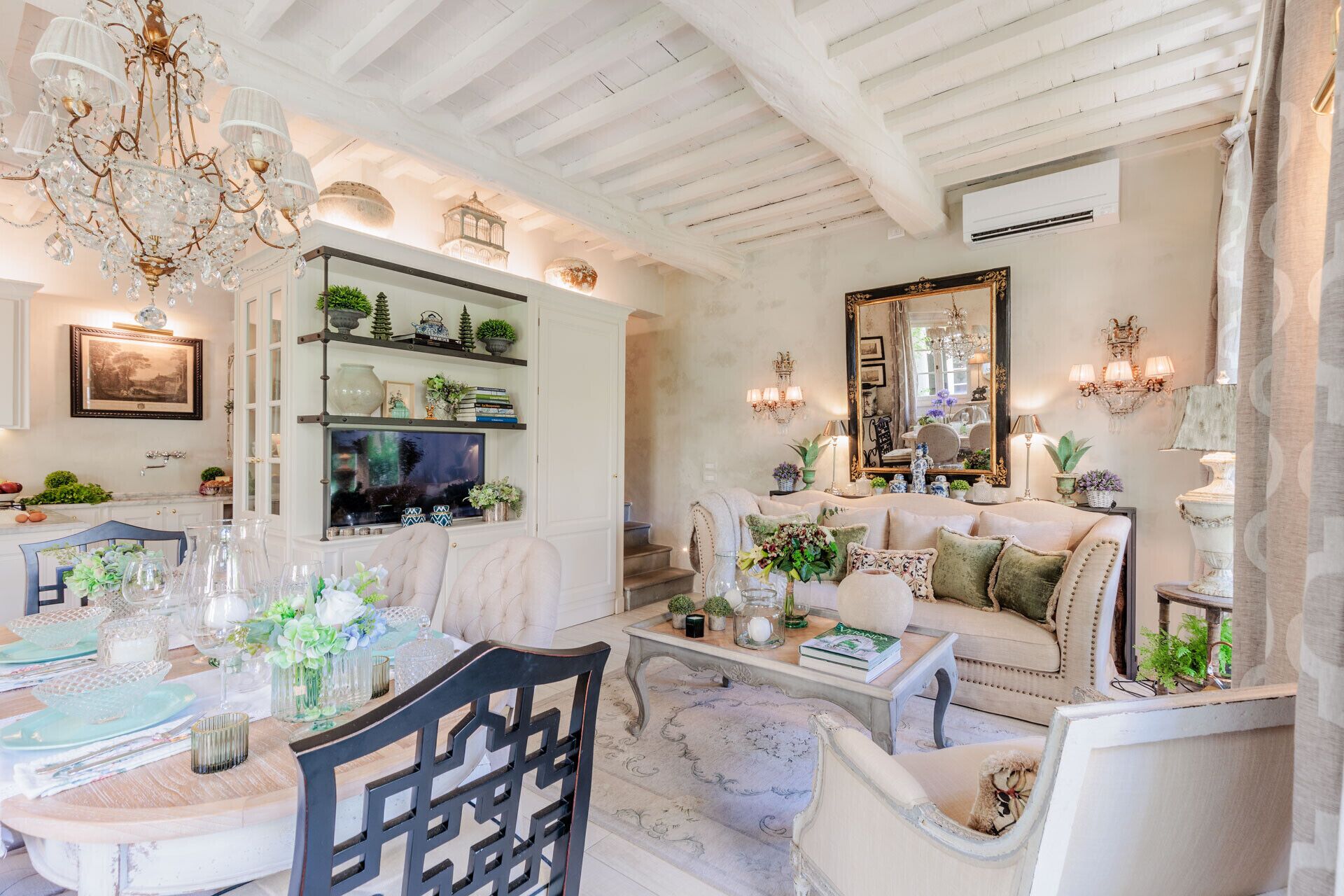 A well-lit room with a chandelier, a television, a sofa, and a dining area with a table set for a meal.