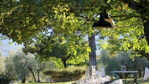 Un espace de restauration en plein air avec une table dressée pour un repas, entourée de chaises et d’un luminaire suspendu.