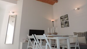 Un coin repas avec une table et des chaises blanches, un plafond en bois et un téléviseur fixé au mur.