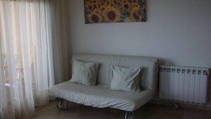 Ein kleines Zimmer mit einem Einzelbett, einem Heizkörper, einem Gemälde von Sonnenblumen und durchsichtigen Vorhängen.