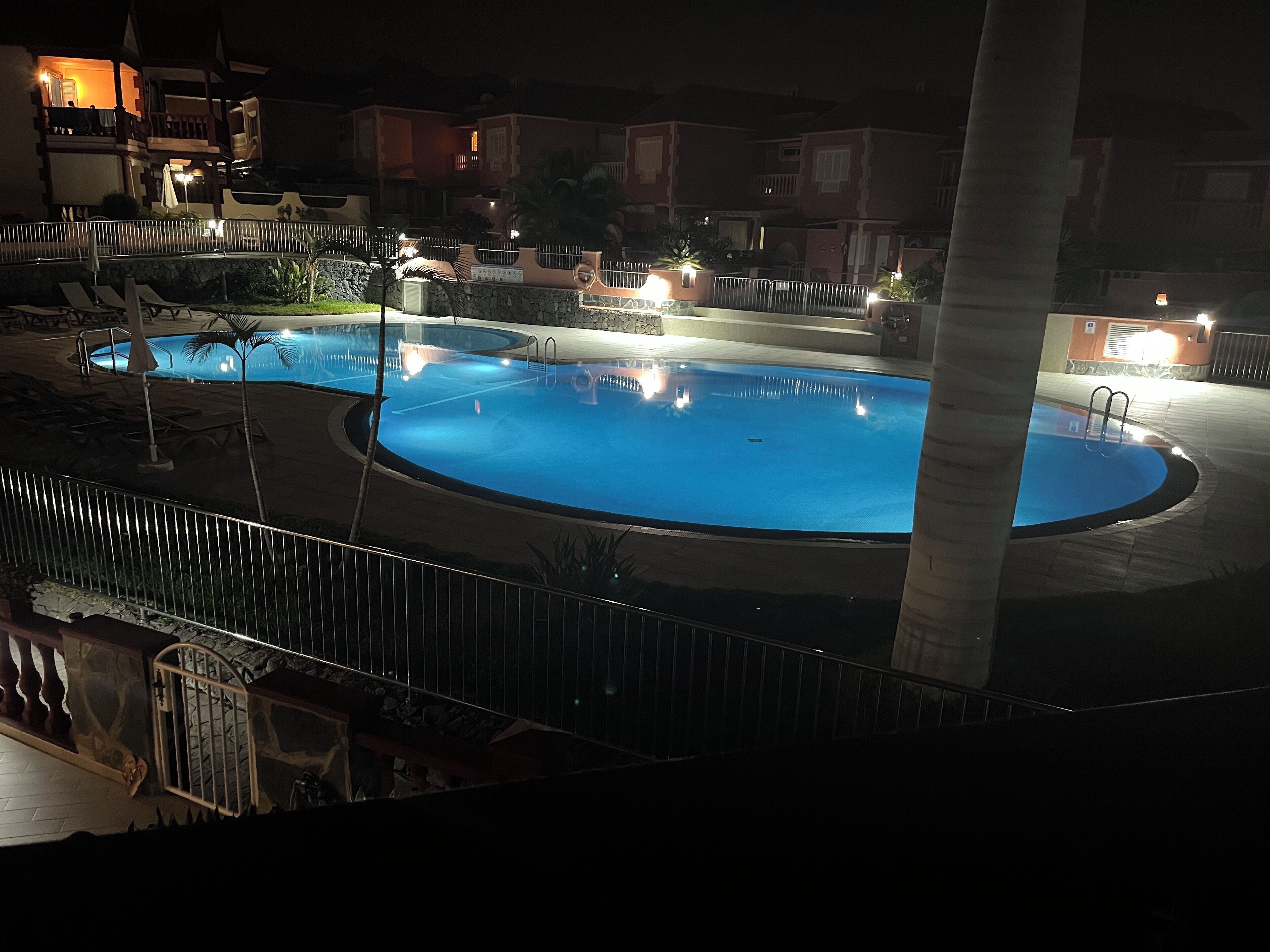 A swimming pool area with lounge chairs and a staircase leading to upper floors.