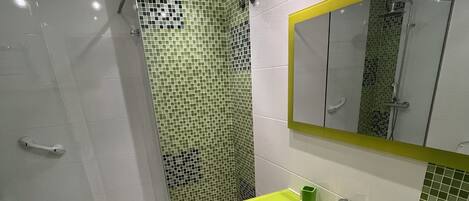 A bathroom with a green sink, white cabinets, a shower with green mosaic tiles, and a green mat on the floor.
