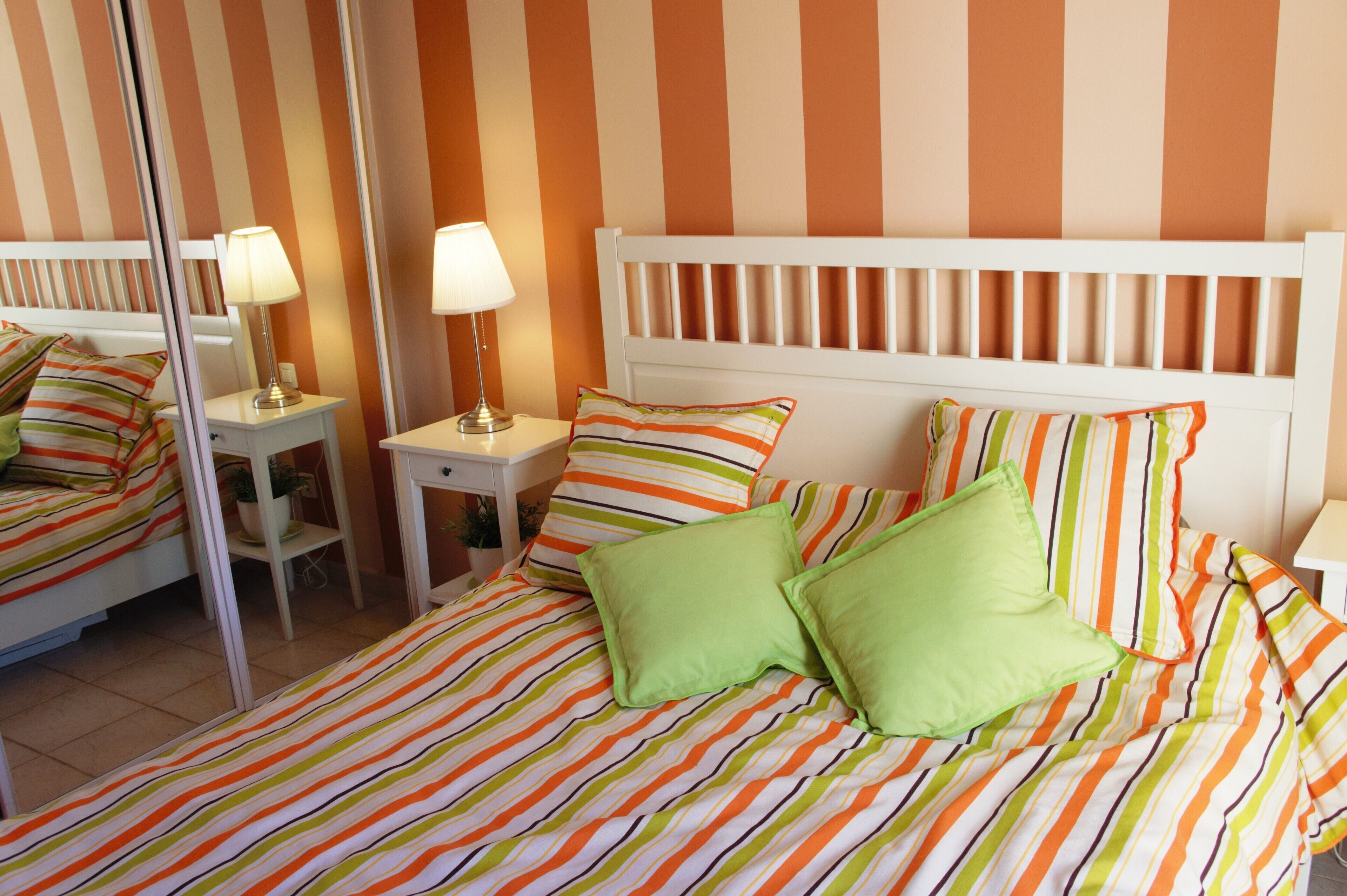 A hotel room with a striped bedspread, a white headboard, and two bedside lamps.