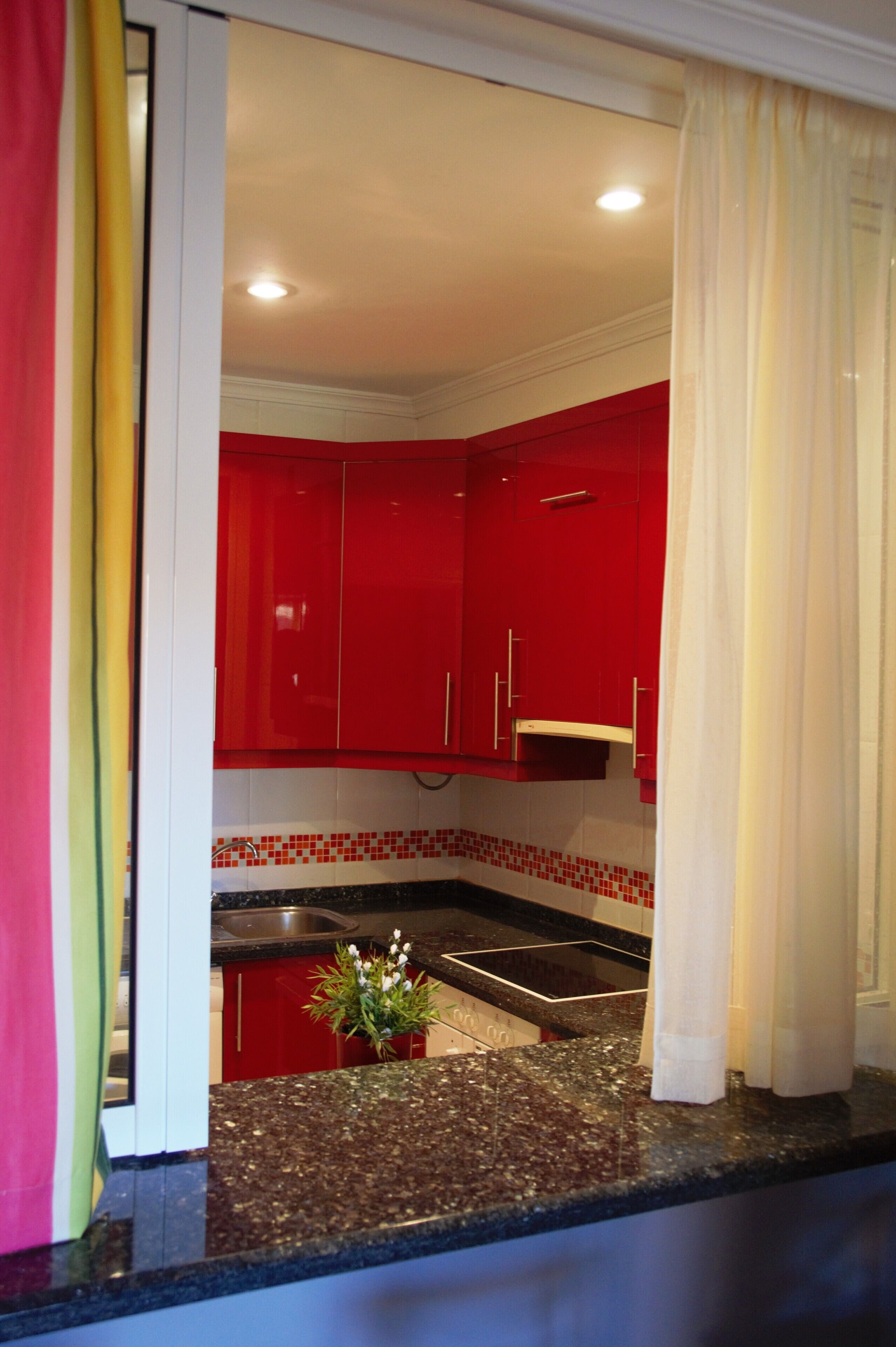 Una cocina con armarios rojos, encimera de granito y una pequeña planta en maceta.