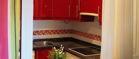 Una cocina con armarios rojos, encimera de granito y una pequeña planta en maceta.