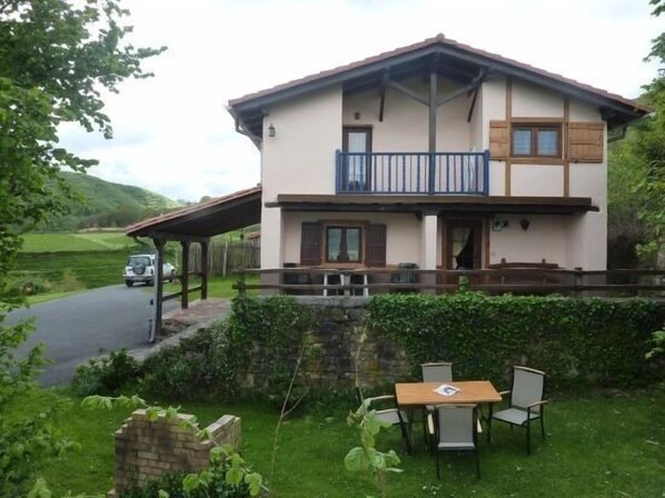 Une maison à deux étages dotée d’un balcon, d’un porche couvert et d’un petit espace extérieur aménagé avec une table et des chaises.