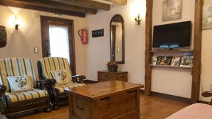 Een gezellige kamer met gestreepte fauteuils, een houten bijzettafeltje, een televisie en een plank met boeken.