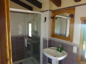 Une salle de bain avec une douche à parois de verre, un lavabo sur colonne et un miroir encadré en bois.