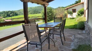 Une terrasse extérieure avec une table et des chaises, offrant une vue sur un paysage verdoyant et des collines.