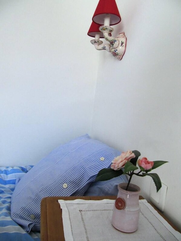 A small room with a bed, a blue striped pillow, a vase with a pink flower, and a red lamp on the wall. - Seaside villa, 100 m from the beach, large garden, 3-star rating (Carnac)
