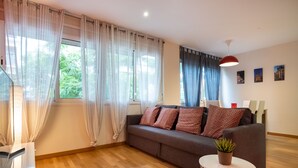 Una sala de estar moderna con un sofá gris, una mesita redonda blanca con una planta y una lámpara colgante roja.