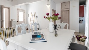 Un coin repas avec une table blanche, des chaises, un vase de fleurs et un lustre.