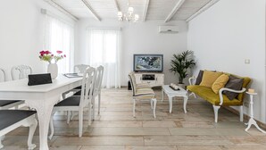 Een eetruimte met een witte tafel, stoelen en een televisietoestel op een kast.