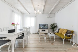 Un coin repas avec une table blanche, des chaises et un téléviseur posé sur un meuble.