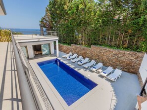 Ein Pool auf dem Dach mit Liegestühlen, einem Glastür-Eingang und einer Steinwand.