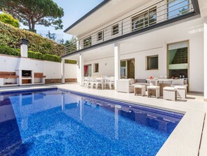 Et moderne hus med swimmingpool, udendørs møbler og en overdækket terrasse.