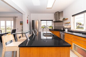 A modern kitchen with a central island, stainless steel appliances, and a large window offering a view of the outdoors. - Villa Farol - Villa in Algarve at walking distance to beach, with pool and fast WiFi (Sagres)