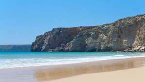 Ein Strand mit einer felsigen Klippe und klarem, blauem Wasser.