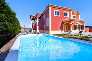 Una casa de dos pisos con piscina, balcón y césped bien cuidado.