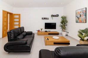 A modern living room with a black leather sofa, a wooden coffee table, a flat-screen TV, and potted plants. - Villa Farol - Villa in Algarve at walking distance to beach, with pool and fast WiFi (Sagres)