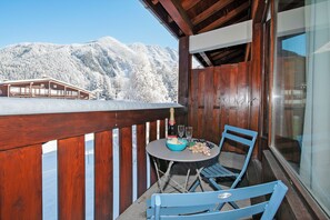 Un balcon avec une balustrade en bois, une table avec une bouteille, des verres et un bol de raisins.