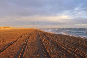 A beach with a sandy path leading to the water, under a cloudy sky.