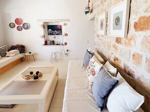 Ein gemütliches Wohnzimmer mit einer Couch, einem Couchtisch, einem kleinen weißen Hocker, einem Regal mit Büchern und Dekoration sowie einer Steinwand.