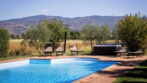 Une piscine dotée de chaises longues et d’un jacuzzi, entourée d’arbres et avec des collines en arrière-plan.