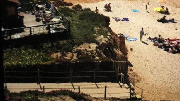 Een strand met mensen die zonnebaden en zwemmen. Er is een gebouw met een balkon dat uitkijkt over het strand.