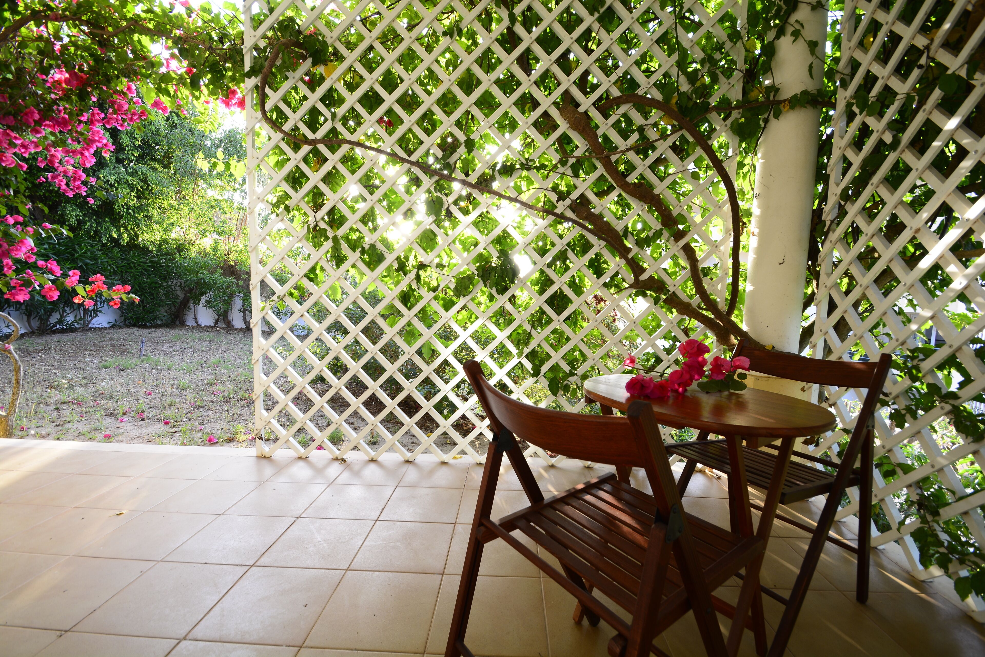 Un conjunto de mesa y sillas de madera en un jardín con cerca de celosía blanca y follaje.