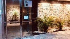 Entrada de un edificio moderno con puerta de cristal, pared de piedra y un letrero que dice 'Abedules 3'.