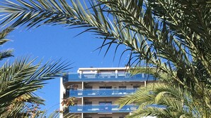 Un edificio de varios pisos con balcones, rodeado de palmeras y otra vegetación.