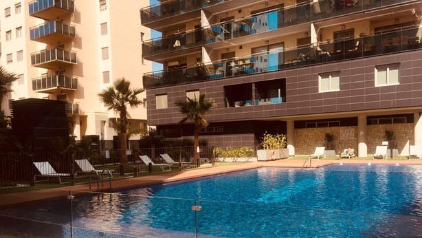 Una piscina con borde de azulejos, rodeada de sillas de descanso y palmeras.