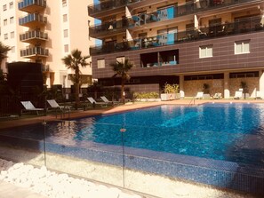 A swimming pool with a tiled edge, surrounded by lounge chairs and palm trees.
