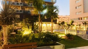 Un hotel de varios pisos con balcones, un jardín bien cuidado con palmeras y un camino pavimentado.