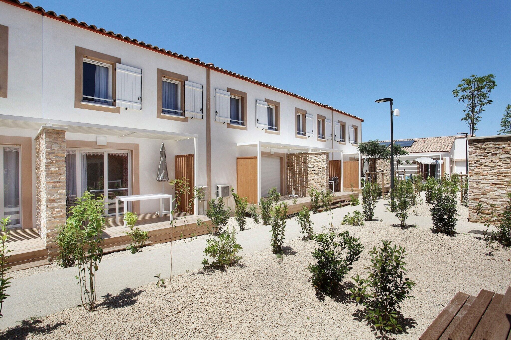 Um edifício moderno de dois andares com um pátio, apresentando uma combinação de paredes de pedra e estuque, diversas janelas e áreas de estar ao ar livre.