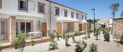Un edificio moderno de dos pisos con un patio interior, que presenta una combinación de paredes de piedra y estuco, varias ventanas y áreas de estar al aire libre.