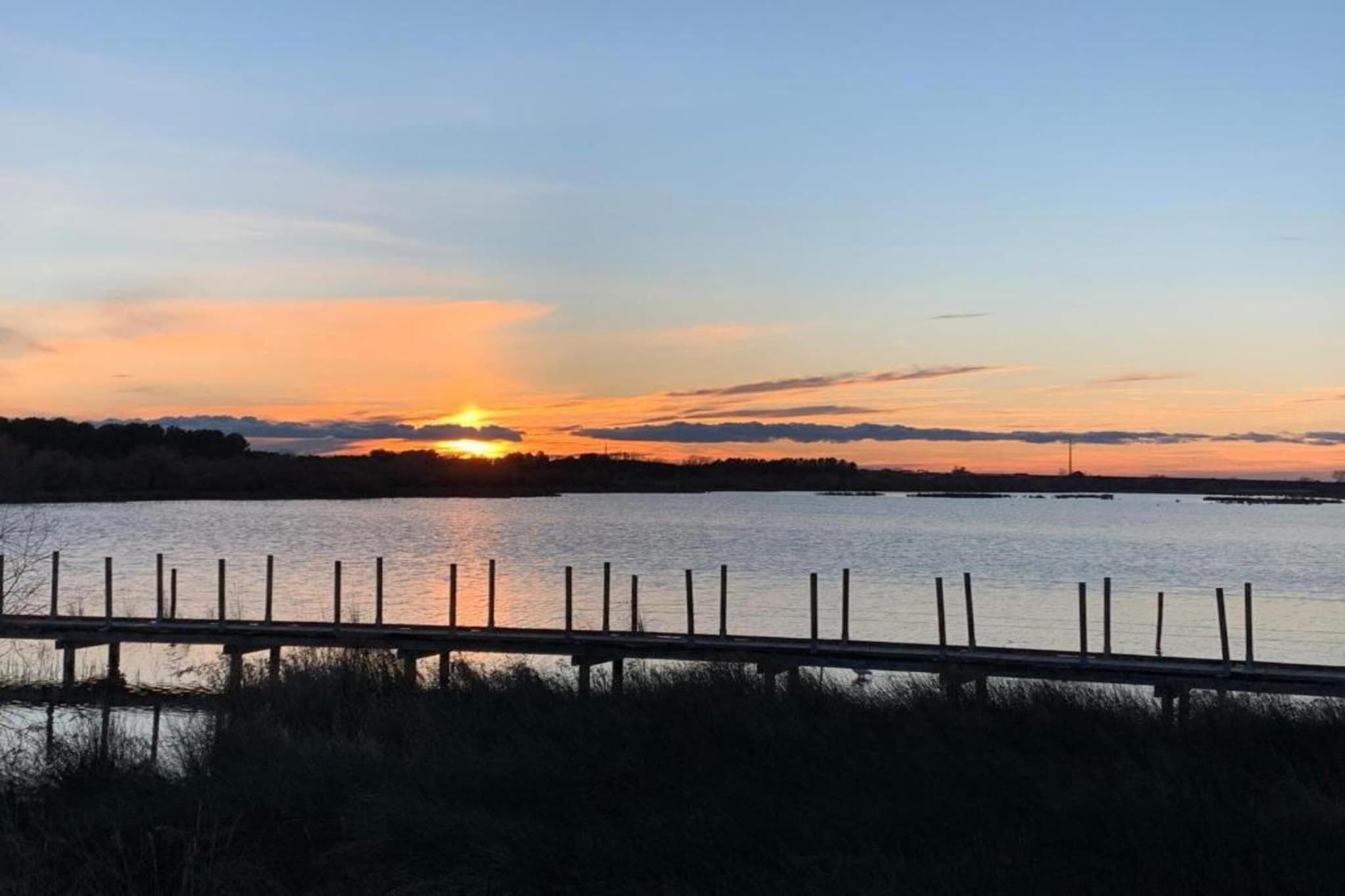 A sunset over a body of water with a wooden fence in the foreground.