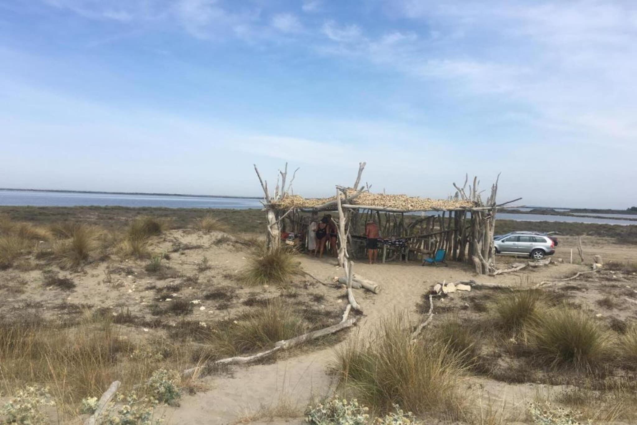 A beach with a simple wooden structure, a car, and sparse vegetation.