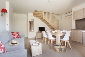 A modern living room with a sofa, dining table, and chairs, a staircase, and a kitchen area. - Maisonette in Aigues-Mortes near Camargue (Aïgues Mortes)