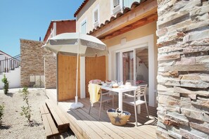 A patio with a table and chairs, a covered umbrella, and a stone wall. - Maisonette in Aigues-Mortes near Camargue (Aïgues Mortes)