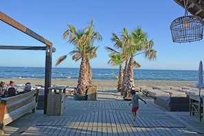 A wooden deck with benches and palm trees overlooking a beach.