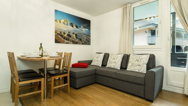 Un salón con un sofá gris, una mesa de comedor con sillas, un cuadro en la pared y una ventana con cortinas.