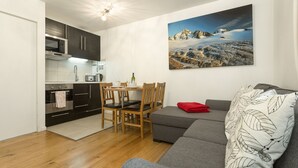 Un espacio habitable compacto con kitchenette, zona de comedor y sofá con un cojín estampado con hojas.
