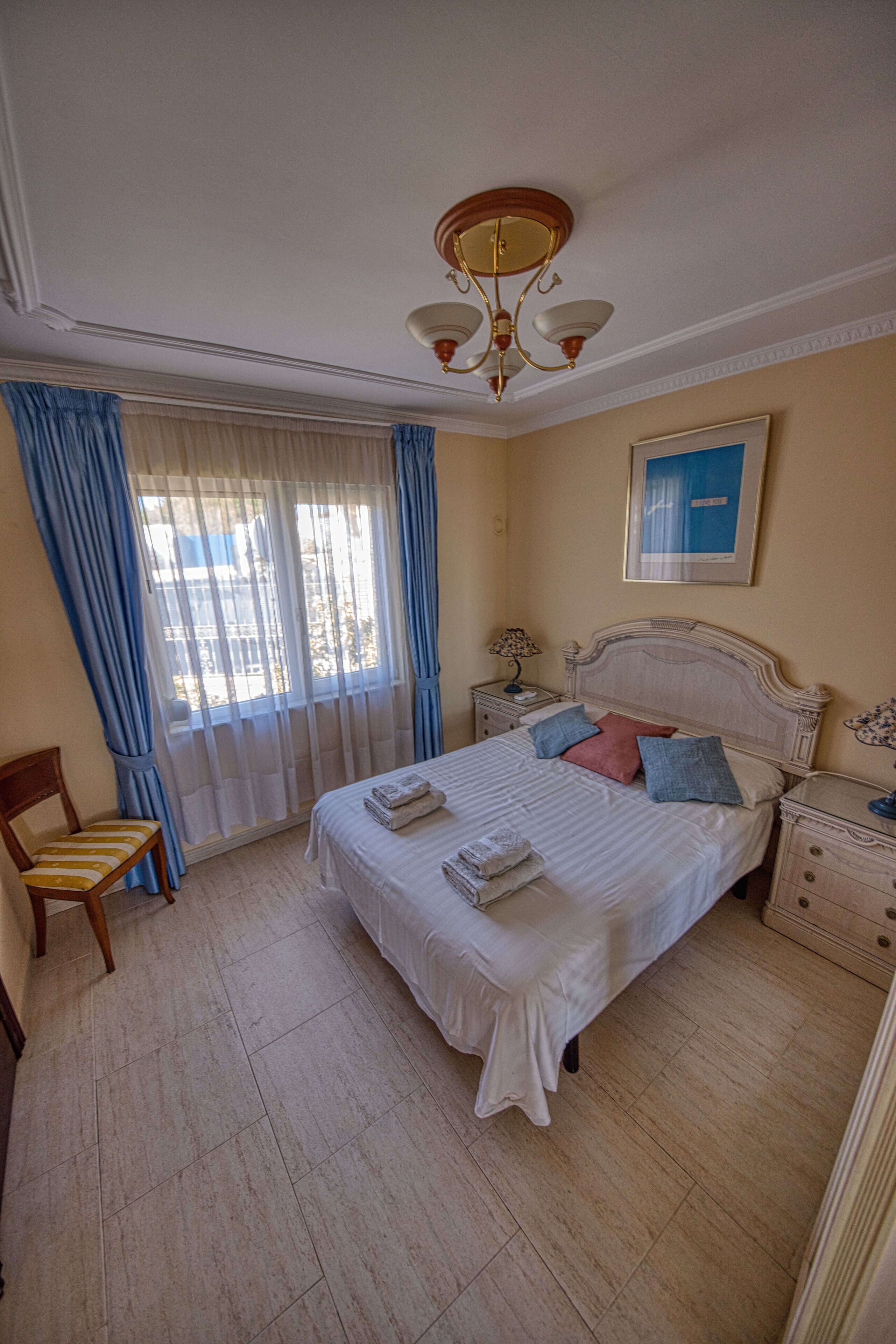 A bedroom with a large bed, a chair, a nightstand, a lamp, and a ceiling light.