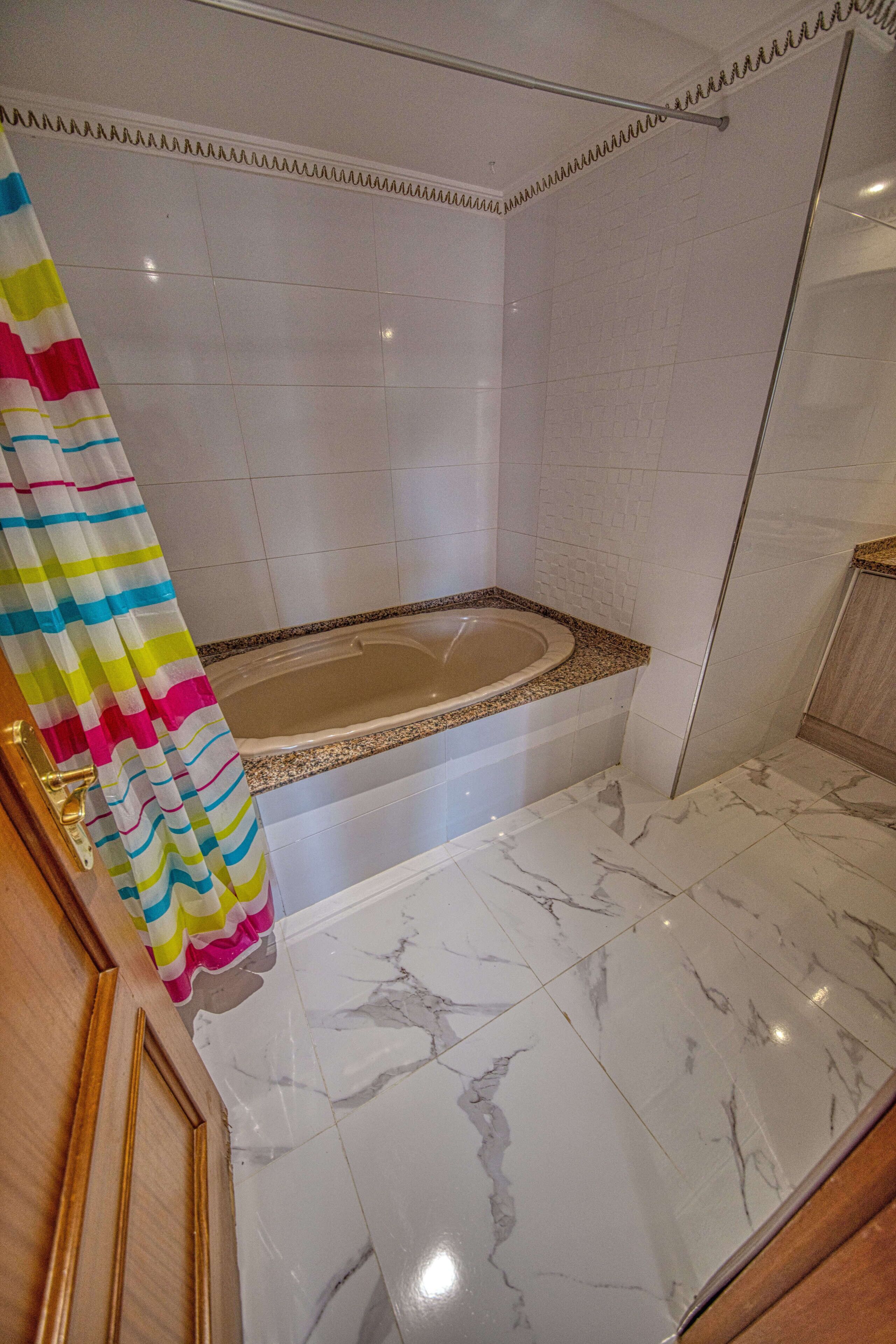 A bathroom with a bathtub, marble flooring, and a shower curtain.