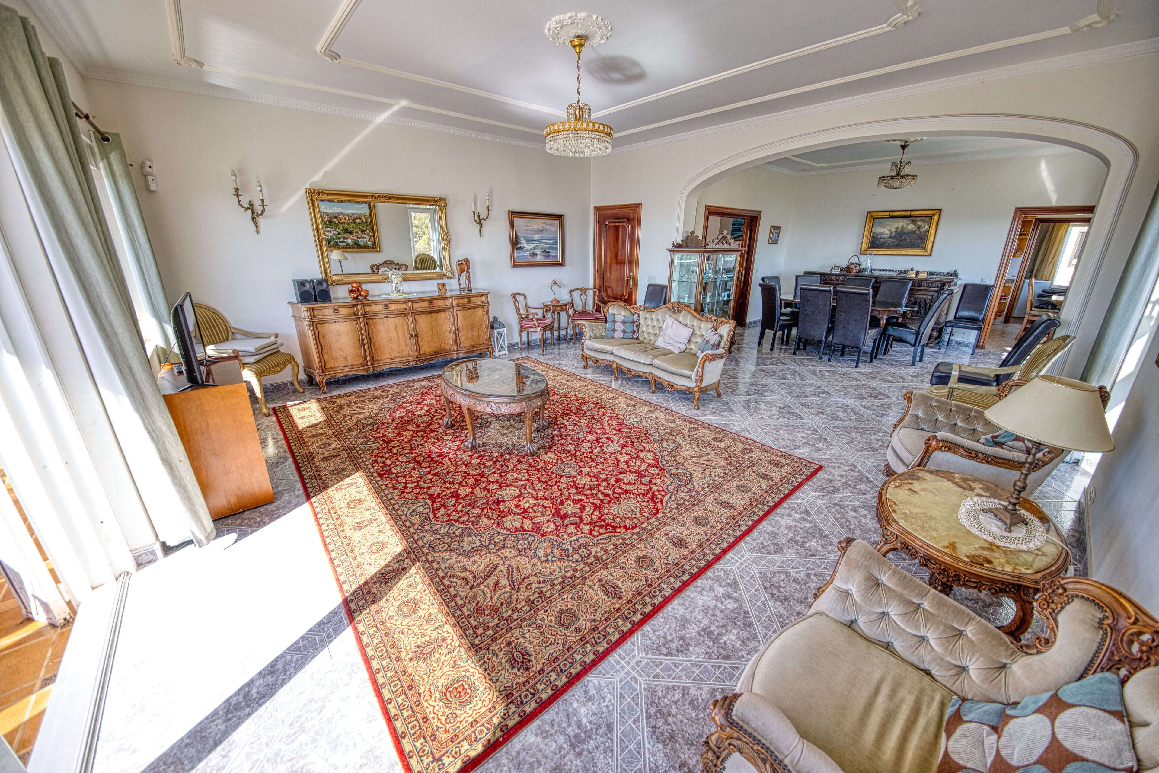 A spacious living room with a large red carpet, elegant furniture, and a chandelier.