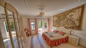 Ein geräumiges Schlafzimmer mit einem großen Bett, einer Sitzecke mit einem Sessel, einem großen Spiegel und Blick ins Freie.
