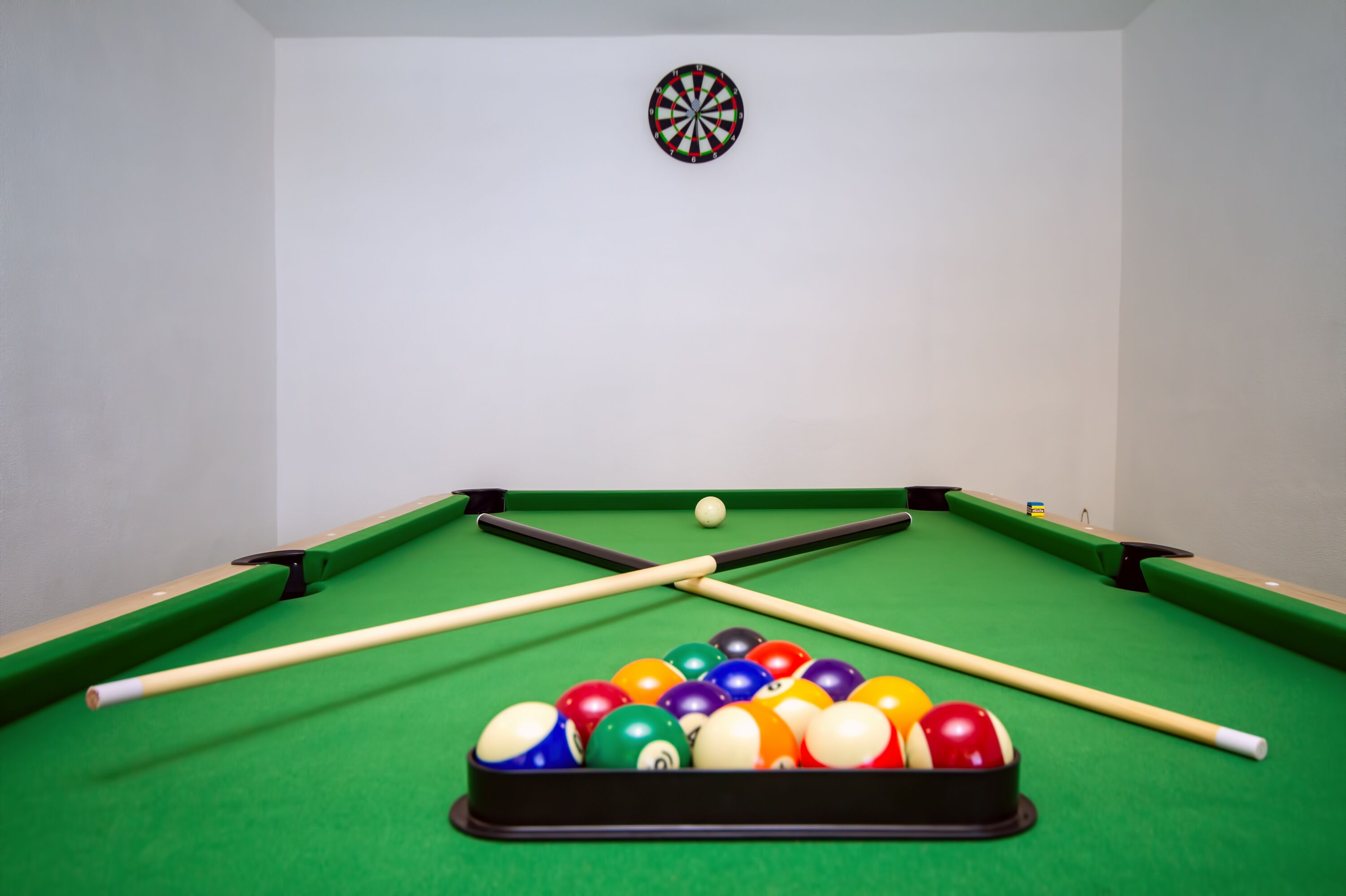 Et poolbord med dartskive og et sæt billardkugler.